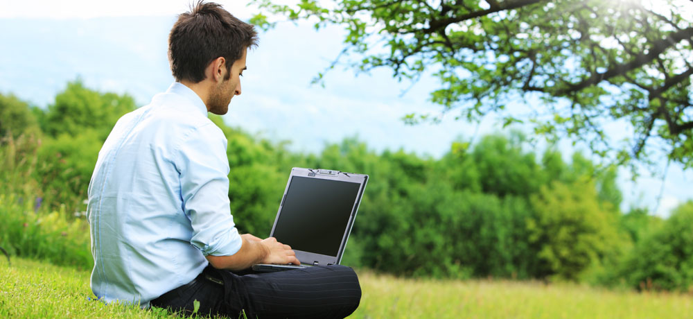 Photo d'un homme assit sur l'herbe travaillant avec un pc portable zen system